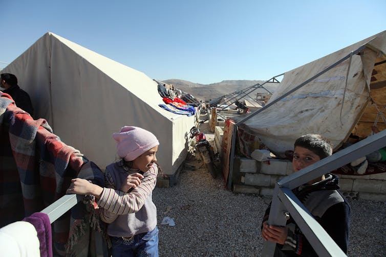 Two children stand outside large tents.