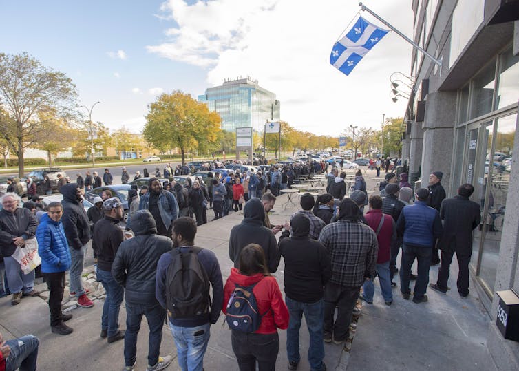 A long line of people outside a building with a Québec flag