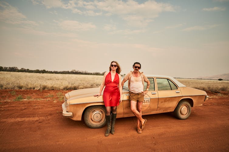 man and woman lean against car in outback