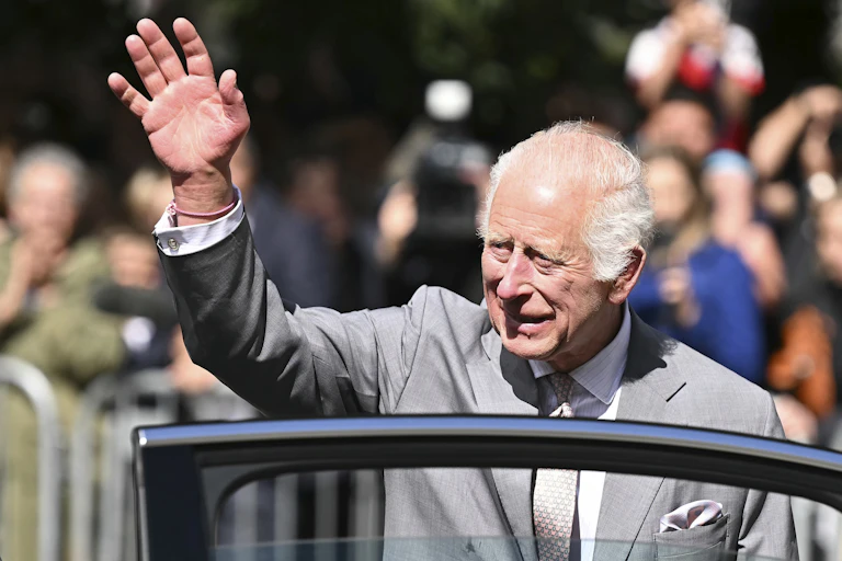 King Charles waves to crowds while stepping out of a car.