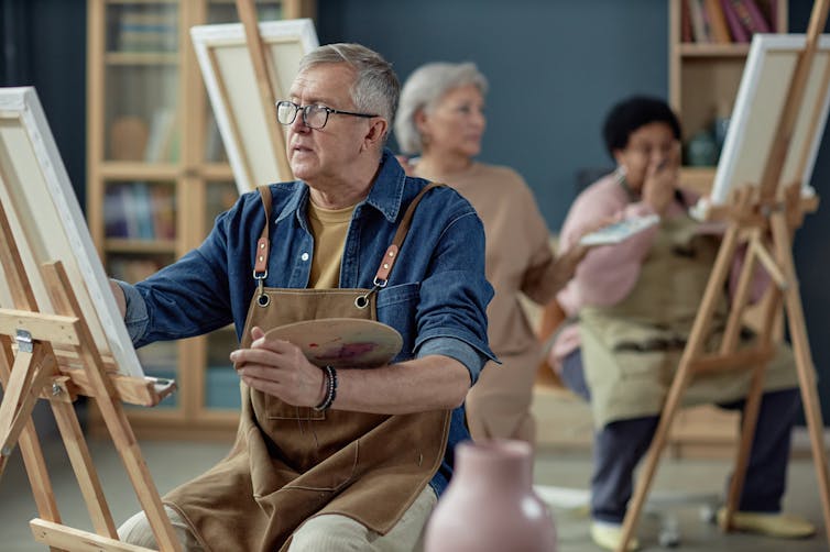 Older man applying paint to a canvas as part of an art class