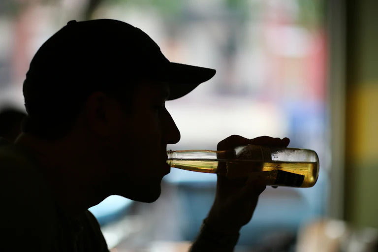 Man wearing cap in silhouette drinking beer out of bottle