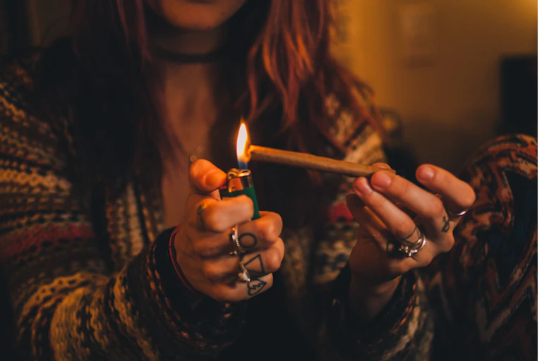 A girl lights a joint with a lighter.