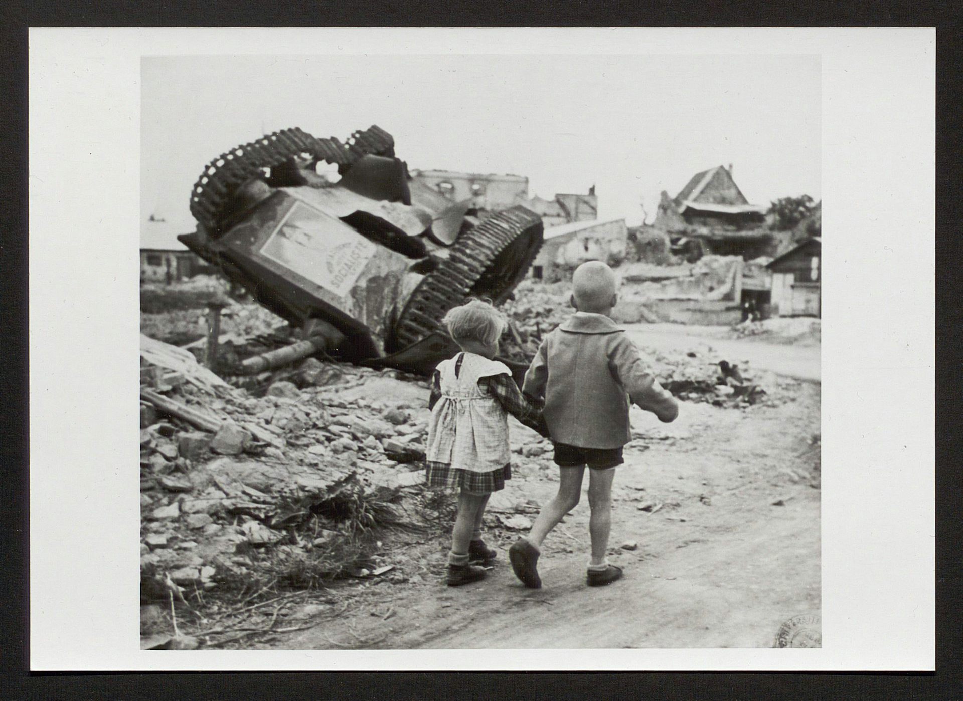 Deux petits enfants passent devant un char renversé