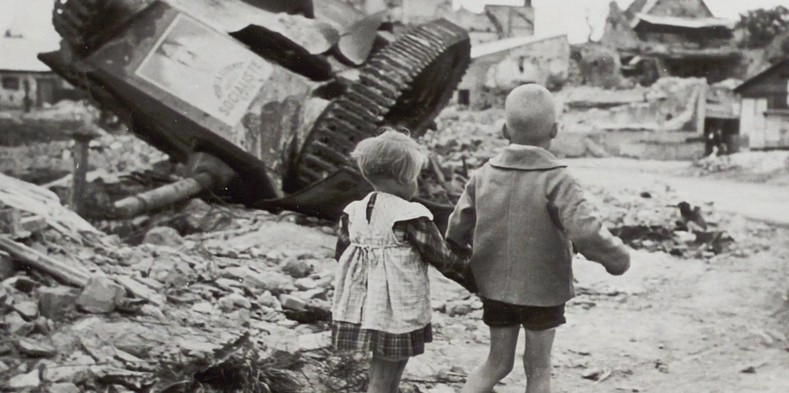 Deux petits enfants passent devant un char renversé