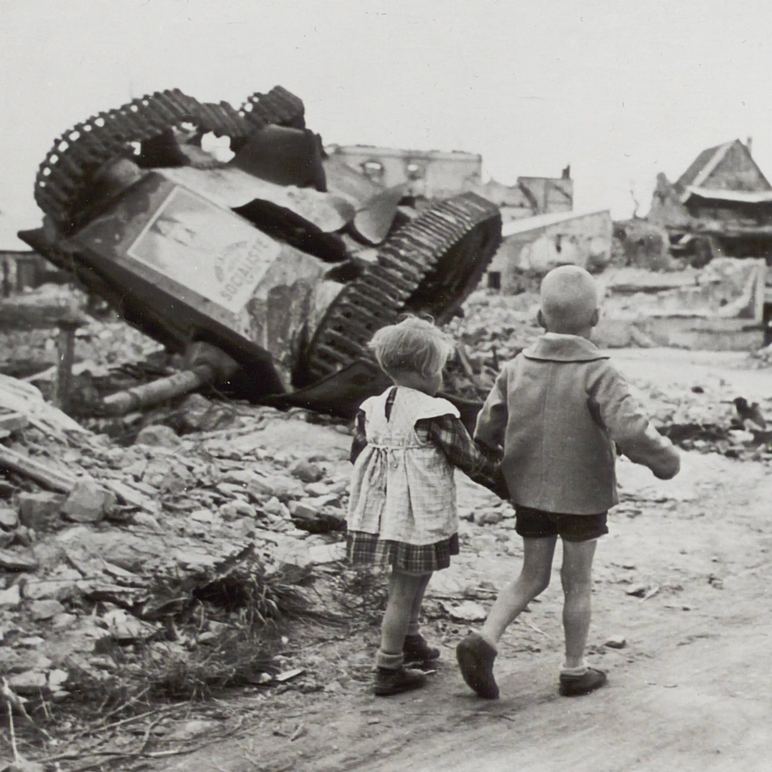 Deux petits enfants passent devant un char renversé
