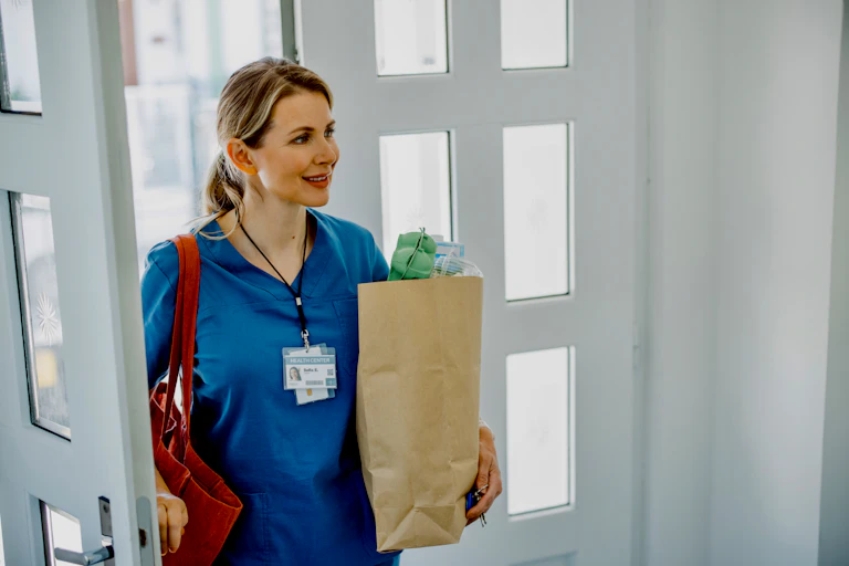 A medical worker returns home carrying a bag of groceries