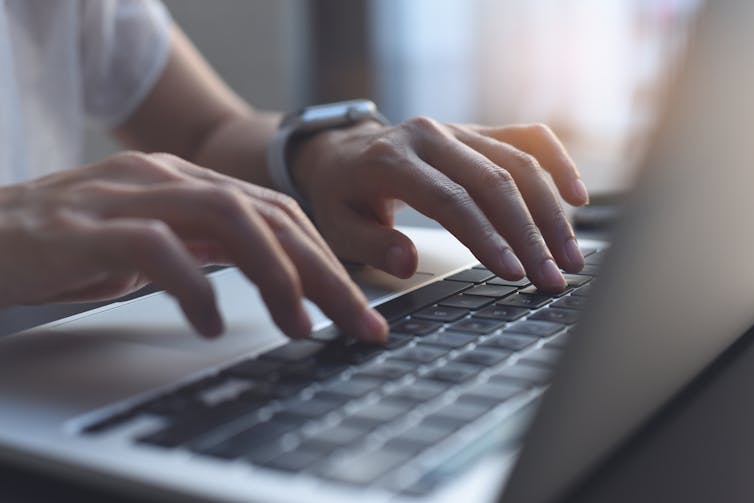 A close up of hands typing on a laptop keyboard.