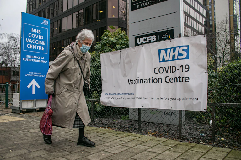 A elderly woman walks past a covid vaccination centre sign in England
