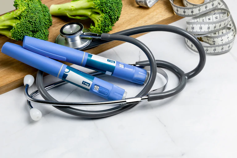 Des stylos d'injection d'Ozempic à côté d'un mètre de couturière, de brocolis et d'un sthétoscope