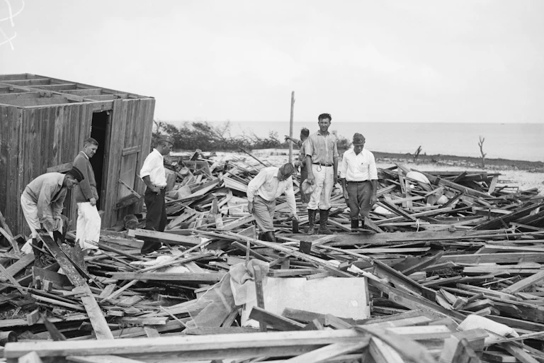 Black and white photo of people standing on debris.