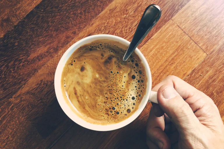 Mão de uma pessoa segura a xícara de café depois de misturar a canela