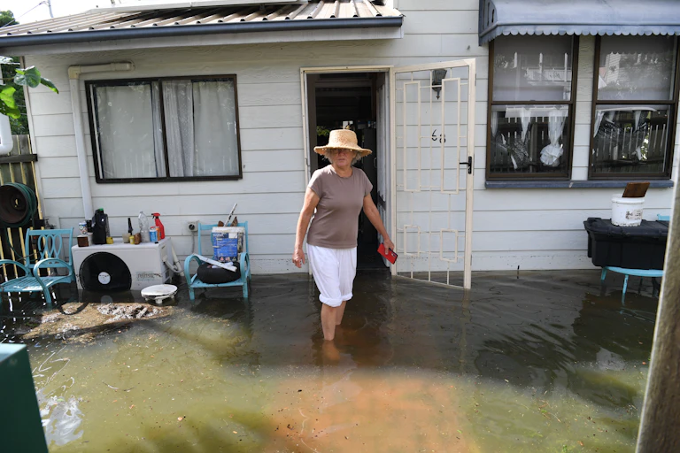 A woman stands in floodwaters outside her weatherboard home in Milton, Queensland