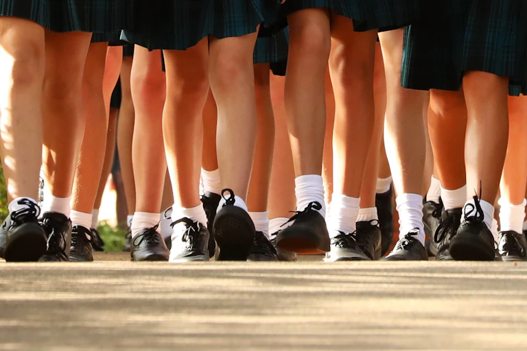 School students in black shoes, with socks and dark shorts/ skirts.