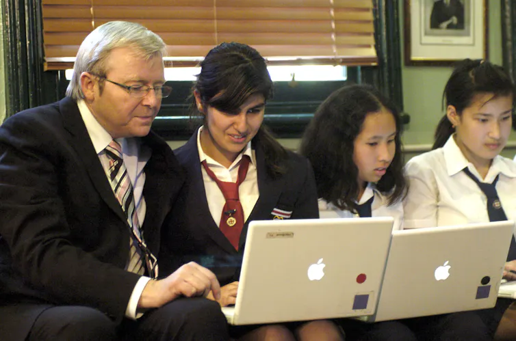 Photo of Kevin Rudd sitting with school students typing on laptop computers.