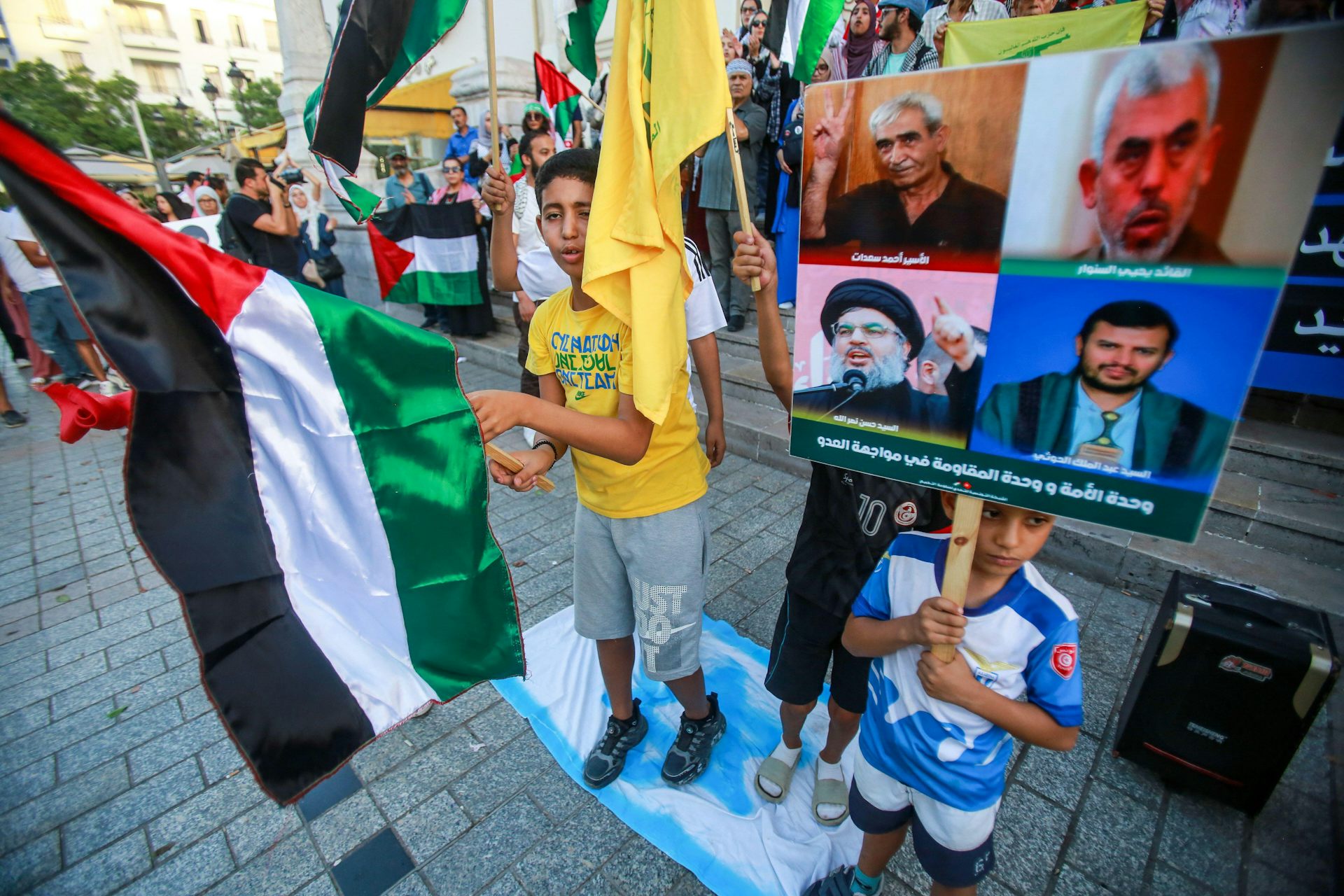 Children in a crowd of protestors holding Palestinian flags and pictures of militant leaders.