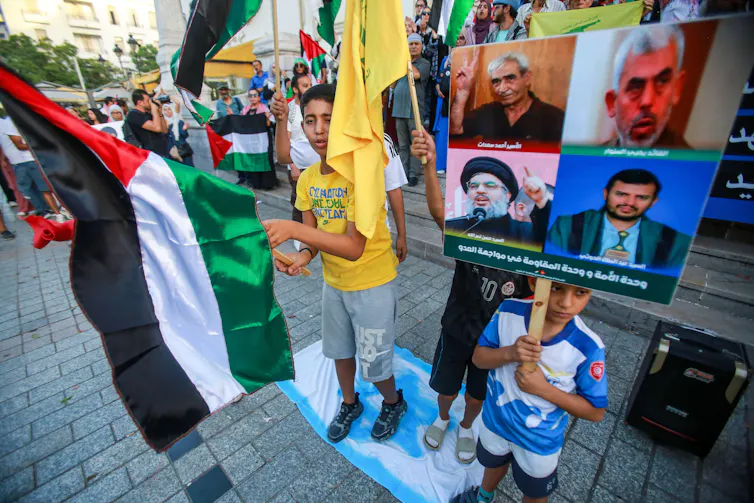 Children in a crowd of protestors holding Palestinian flags and pictures of militant leaders.