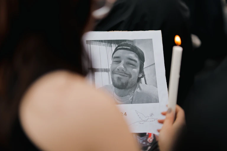 Photo of a fan holding a black and white photo of Liam Payne and a white, lit candle