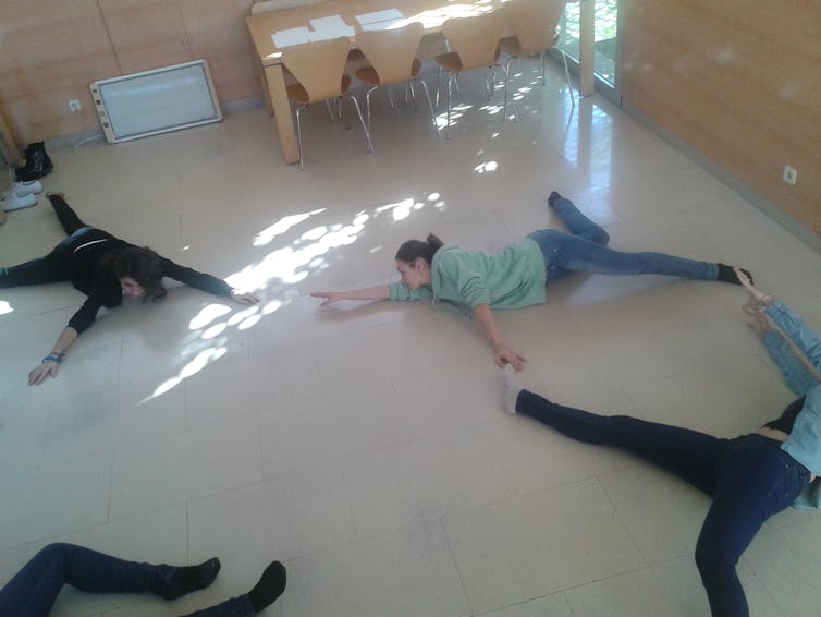 Varios adultos tumbados en el suelo del aula en diferentes posturas.