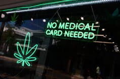 Bright green neon sign hanging in window that says No Medical Card Needed