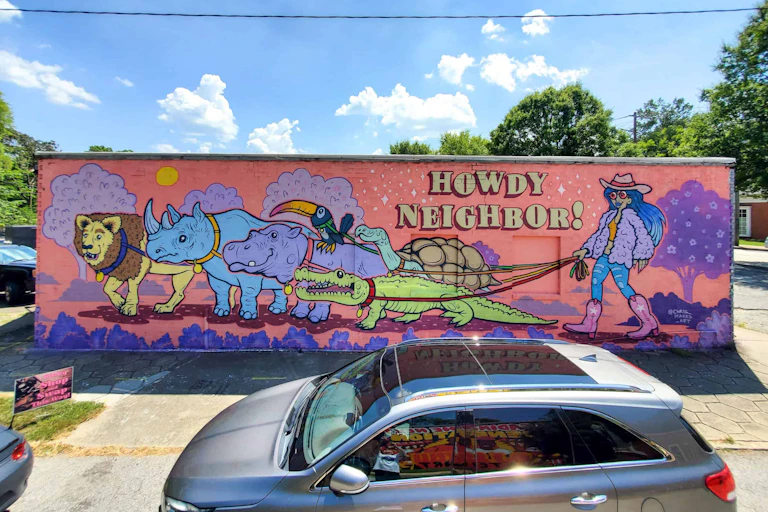 A woman in a cartoon mural captioned 'Howdy Neighbor!' walks an alligator, hippo, rhinoceros and lion on leashes