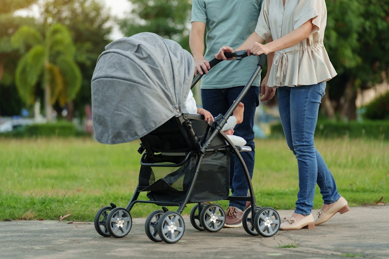 two parents pushing a pram walking in a park