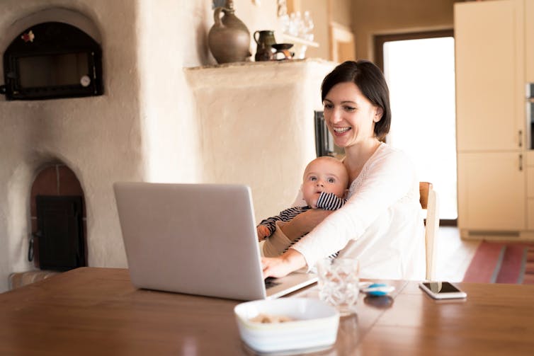 Mother with small baby working from homeoffice, typing on laptop