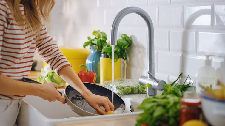 A woman washes a nonstick pan in the kitchen sink.