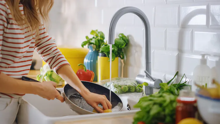 A woman washes a nonstick pan in the kitchen sink.