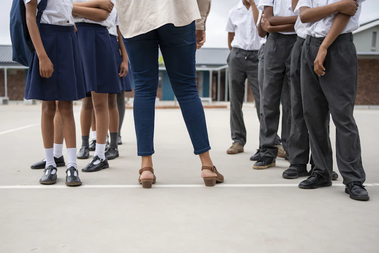 Girls and boys in school uniform, seen from chest down, with an adult standing between them