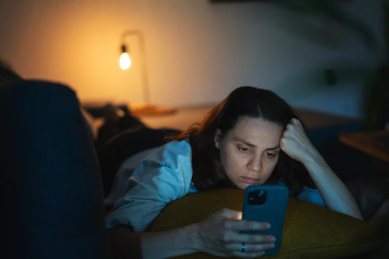 A woman doomscrolls on her smartphone late at night.
