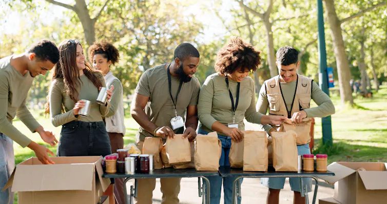 A group of volunteers assemble bags of food outdoors.