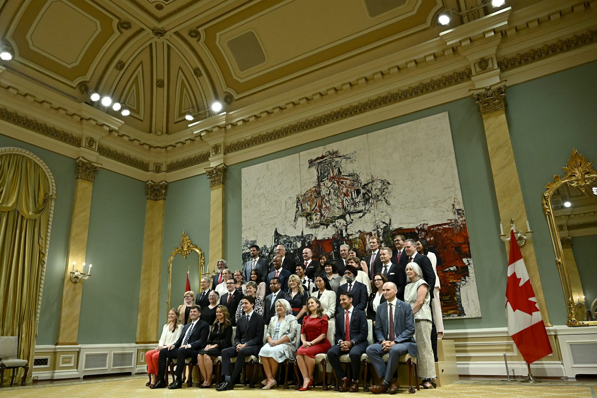 A group stands for a portrait in an ornate room.