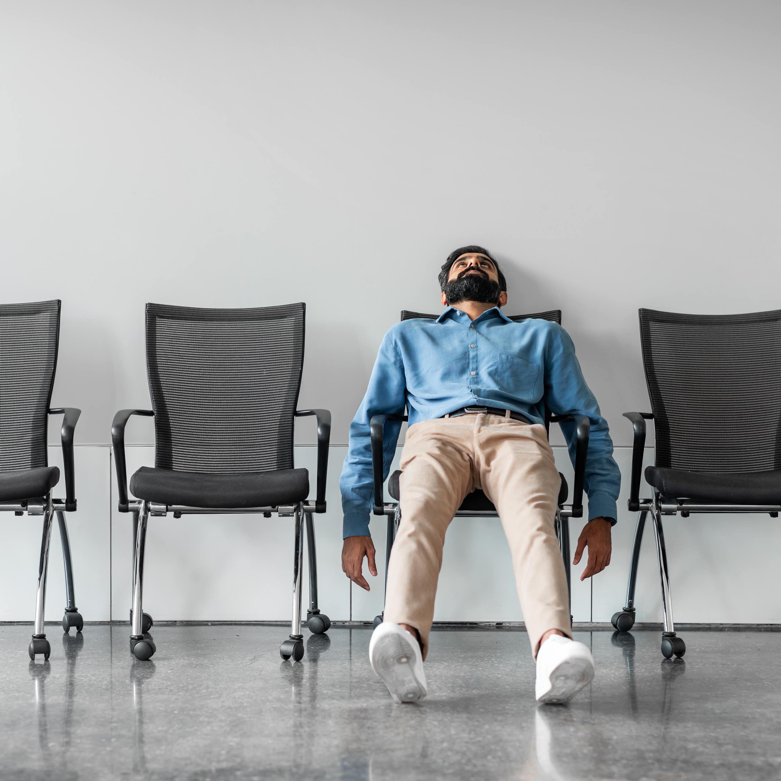 A man slumps in one chair in a row of chairs.