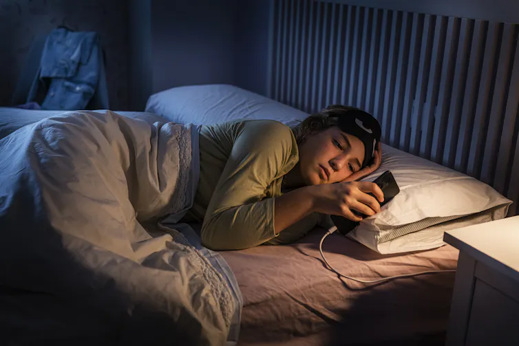 A person lies in bed looking at their smartphone.