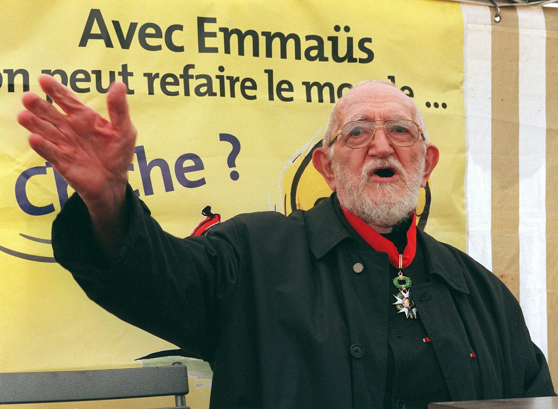 Abbé Pierre in front of an Emmaüs banner.
