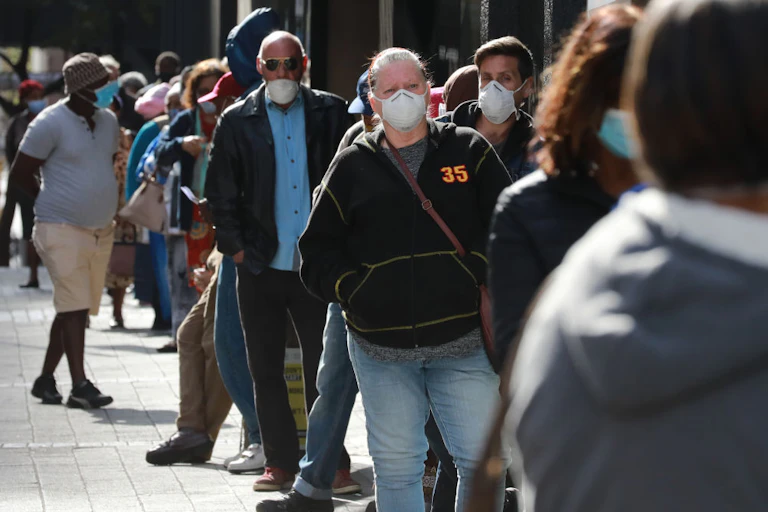 People standing outdoors in a queue, wearing COVID face masks