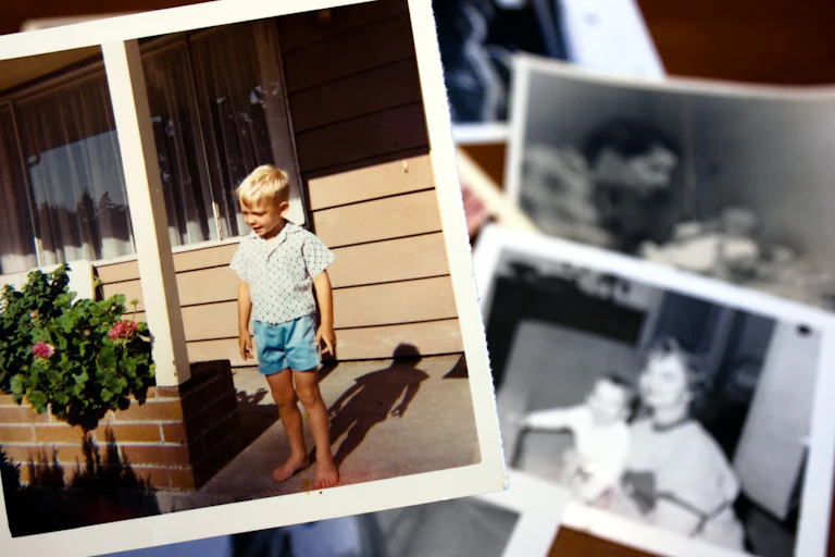 Hand holds a vintage color photograph of young boy standing on a front stoop.