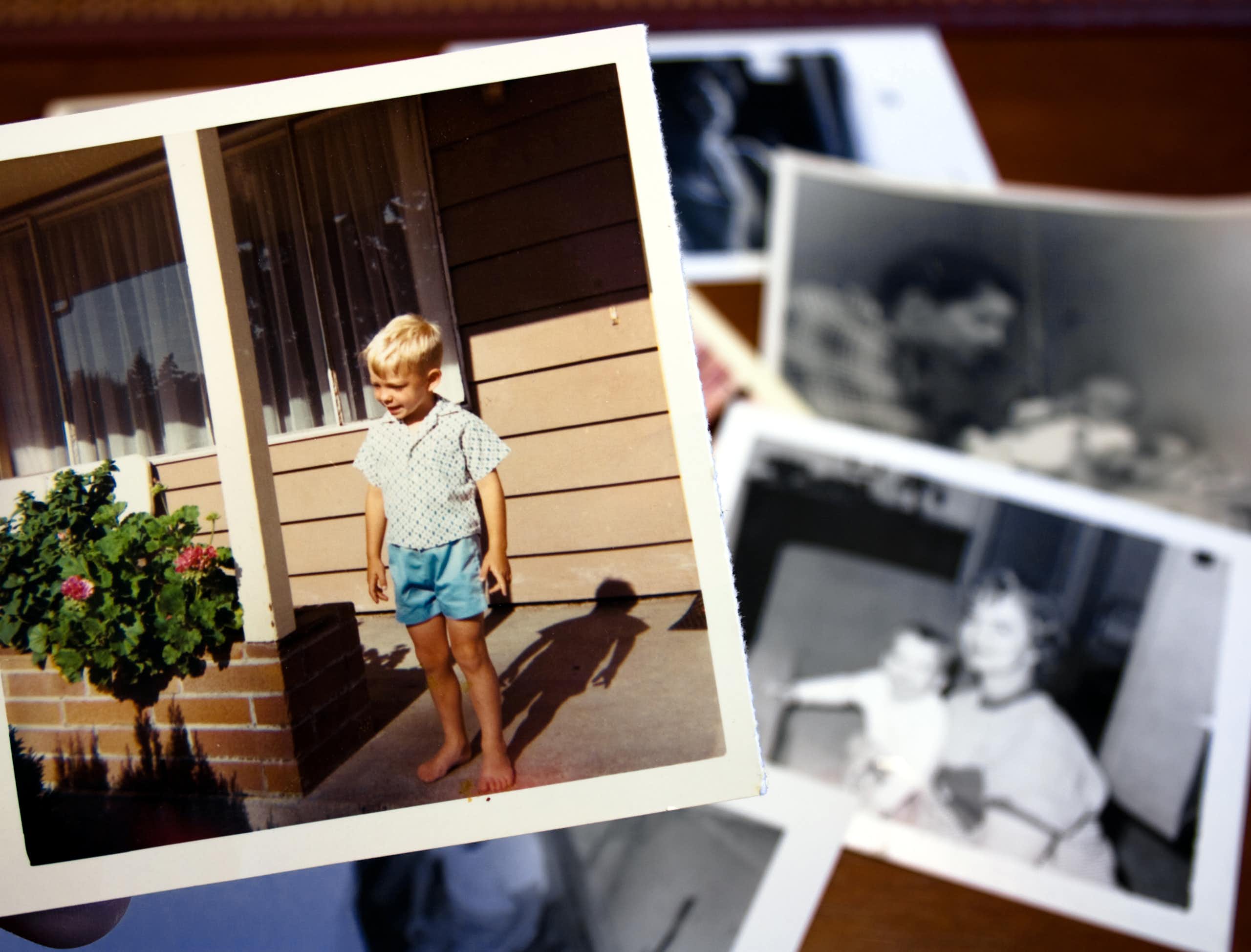 Hand holds a vintage color photograph of young boy standing on a front stoop.