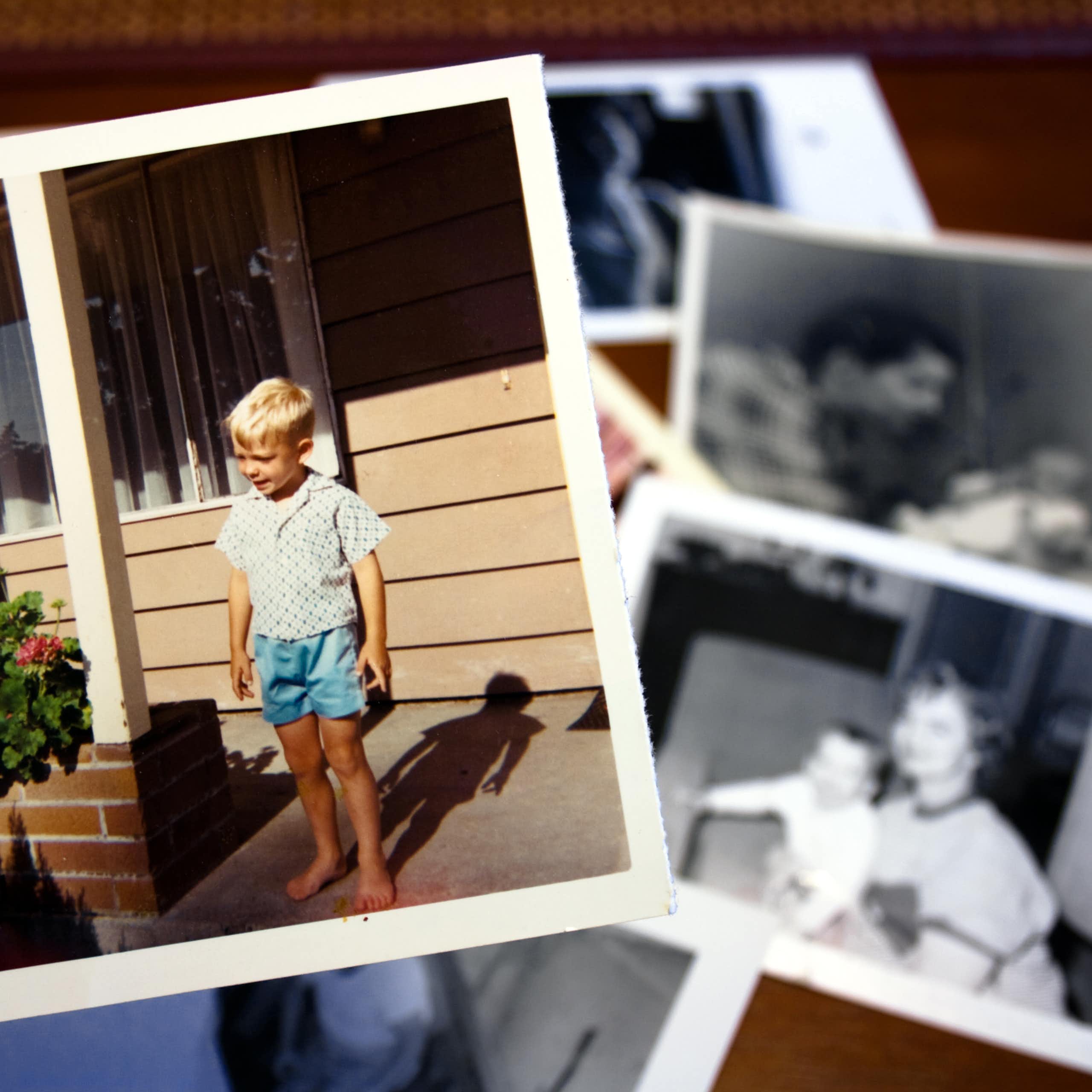 Hand holds a vintage color photograph of young boy standing on a front stoop.