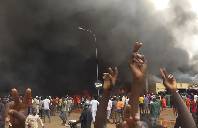 People protest in front of a burning building.