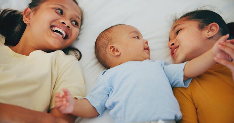 Two older children lying on both sides of a baby.