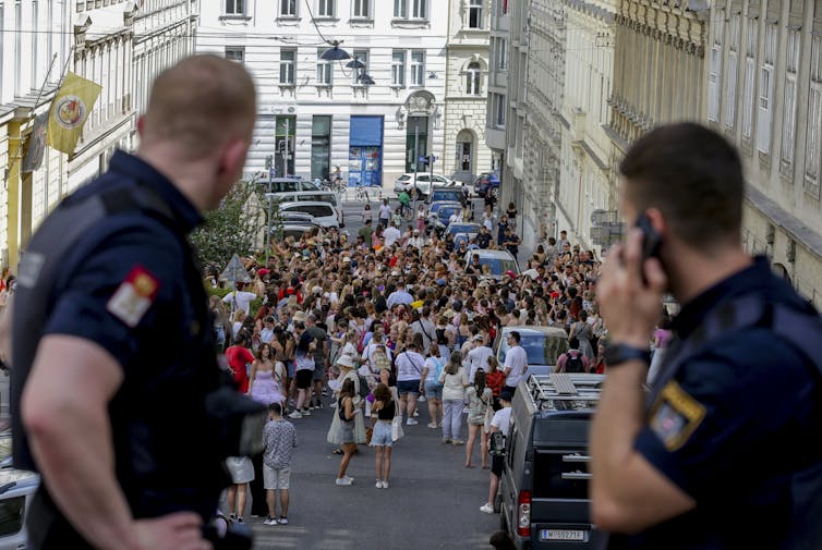 two police officers in the foreground watch a crowd of people in the distance