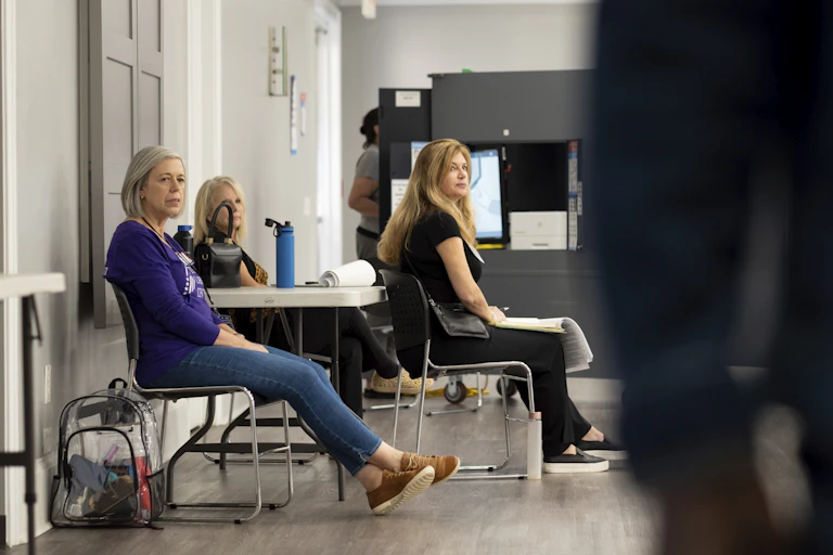 People sit in chairs against a wall.