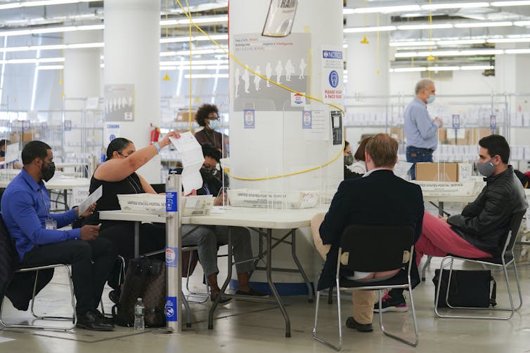 People on one side of a table hold up a piece of paper so people on the other side of the table can see.