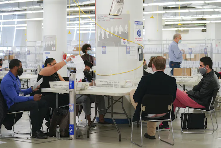People on one side of a table hold up a piece of paper so people on the other side of the table can see.