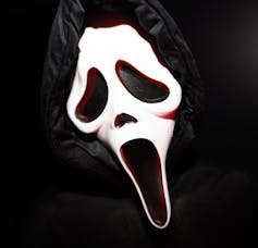 A fan wearing a 'Ghostface' mask, complete with hollowed-out eyes, nose and mouth, and stark white skin.