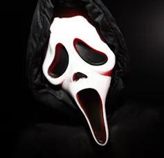 A fan wearing a 'Ghostface' mask, complete with hollowed-out eyes, nose and mouth, and stark white skin.