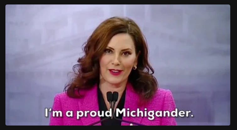 Still of a GIF of woman in bright pink blazer speaking into microphone with text reading 'I'm a proud Michigander' at bottom of image