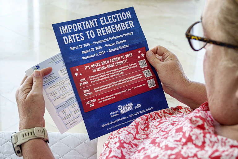 An elderly woman wearing glasses looks at a handout showing important dates in Florida's election